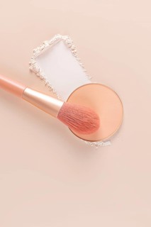 Top view of a makeup brush and compact powder next to loose powder on a beige surface, ideal for