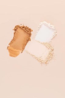 Top view of a split representation of compact and loose face powders, spilled on a beige background
