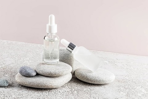 Two glass dropper bottles with clear and frosted finishes are placed elegantly on a stack of