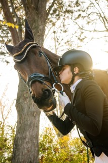 From below teenage girl, dressed in classical dressage attire, is affectionately interacting with a