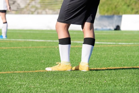 A soccer player stands on a vibrant green soccer field, wearing yellow cleats, black shorts, and