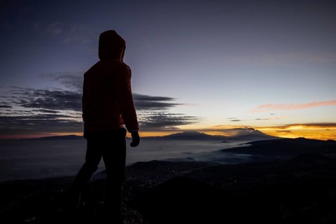 Back view of unrecognizable man standing at the summit during sunrise, overlooking distant