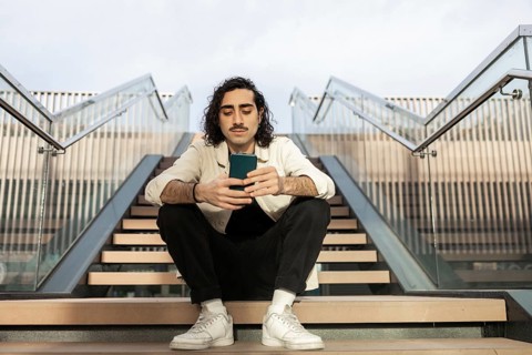 Young man sitting on outdoor stairs, casually browsing his smartphone The setting is urban and