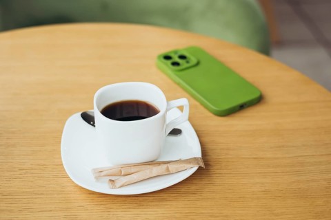 A cozy scene featuring a cup of coffee on a wooden table with a smartphone in a green case The