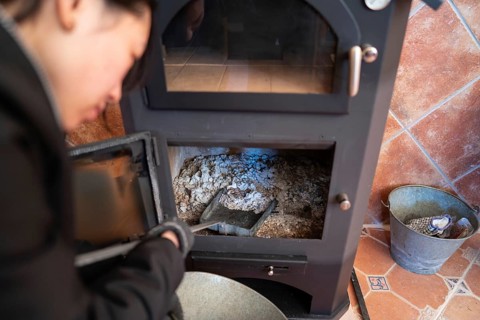 Cropped blurred Asian woman, looking down, is cleaning the ashes from a wood burning stove, holding
