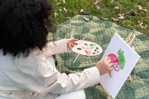 A black woman enjoys painting in a park, capturing creativity on canvas. Surrounded by a peaceful