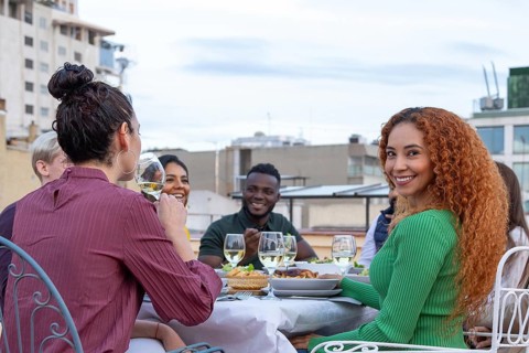 A group of friends enjoying a rooftop party, sharing drinks, food, and laughter under a clear sky