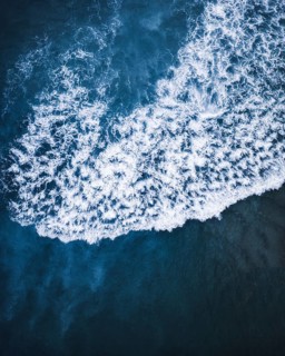 A breathtaking aerial shot of white ocean waves crashing against deep blue waters on the coast of