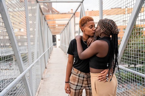 An LGBT multiethnic couple shares a tender embrace and kiss on a lively urban bridge. The vibrant