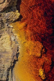 Striking aerial view of the Riotinto River, capturing its vibrant red and orange hues meeting rocky
