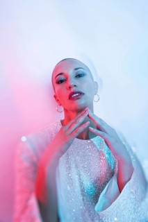 Middle-aged woman with shaved head in stylish pose, adorned with intricate attire. Artistic