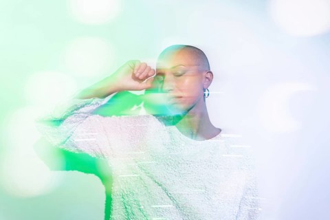A serene image of a middle-aged woman with a shaved head, wearing a textured white top against a