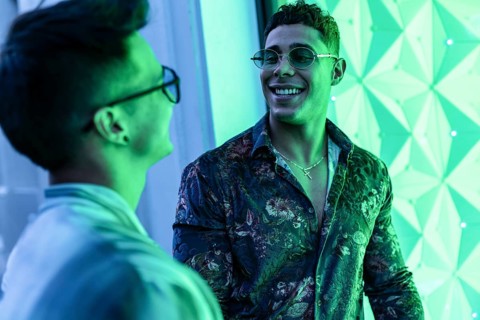 Two latin gay men smiling warmly at each other in an illuminated urban setting. Vibrant green tones