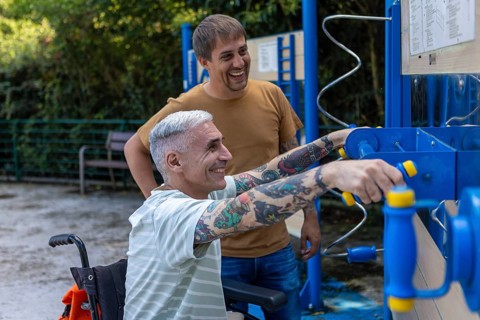 Two men enjoy a sunny day in the park, using accessible outdoor exercise equipment The man in a