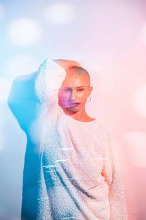 Middle-aged woman with shaved head poses confidently in creative lighting. The colorful bokeh