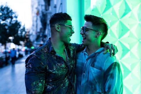 Latin gay couple enjoying an evening in the city, sharing laughter and embracing under vibrant neon