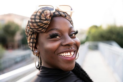 Vibrant portrait of a young black woman with a patterned headscarf and sunglasses, smiling brightly