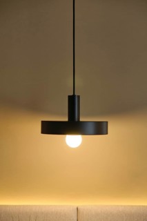 A modern hotel room showcases a sleek pendant light against a warm, neutral wall. The glowing bulb