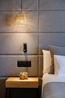Elegant hotel room features a woven pendant light, modern upholstered wall, sleek bedside table
