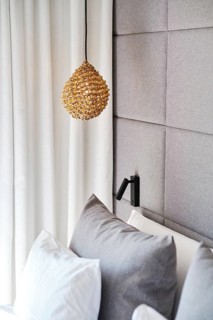 A cozy hotel room with a woven pendant lamp, plush gray pillows, and a textured gray upholstered