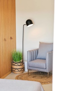 A cozy hotel room corner featuring a gray armchair, woven basket with green plant, and a sleek