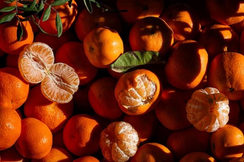 A collection of vibrant tangerines with some peeled, showcasing their juicy segments. Sunlight and