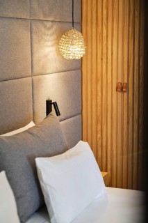 A modern hotel room features soft gray bedding, ambient pendant light, and vertical wood accents,