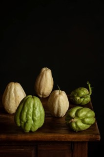 A rustic display of fresh chayote on a dark wooden table against a black background. The vegetable