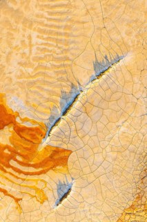 Aerial view of cracked mud in vibrant hues, showcasing an abstract pattern of orange, blue, and