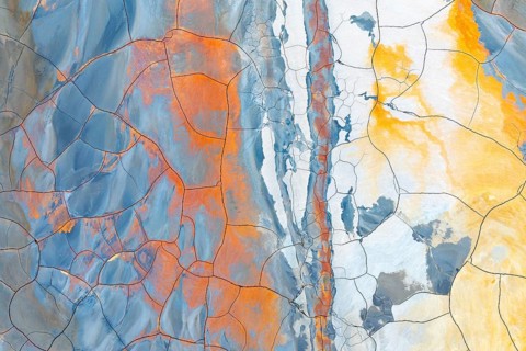 Aerial view of multicolored cracked mud showing vibrant hues of blue, orange, and yellow This