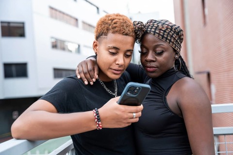 A loving multiethnic couple stands close, sharing a moment while looking at a smartphone. They