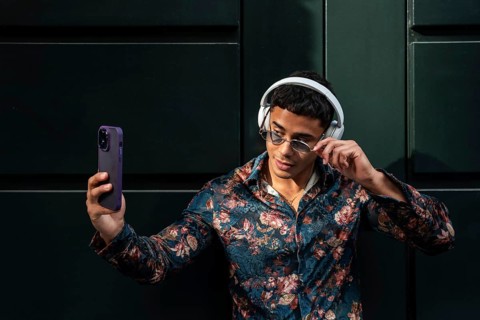A trendy latin man in floral shirt and sunglasses takes a selfie outdoors, showcasing modern style