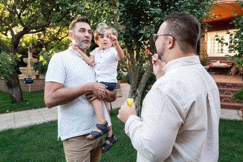 A gay couple enjoys a sunny afternoon in the garden with their young son, creating bubbles and