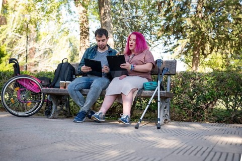 A college couple sits on a bench, studying with clipboards The woman, managing a disability due to