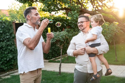 A heartwarming scene shows a gay couple cherishing playful moments with their son outdoors. One