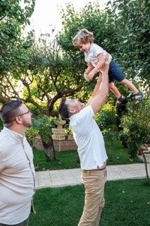 A loving gay couple enjoys quality time with their cheerful son in a lush garden setting. One