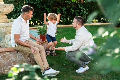 Joyful scene of a gay couple with their son in a lush garden. One father encourages their jumping
