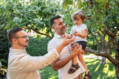 A joyful scene of a gay couple spending quality time with their young son outdoors. They are in a