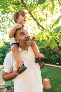 A cheerful father and his young son enjoy a sunny day in the garden. The father carries the child