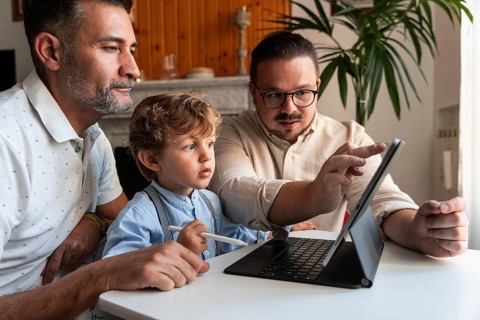 A loving gay couple enjoys quality time with their young son while using a tablet. The family is