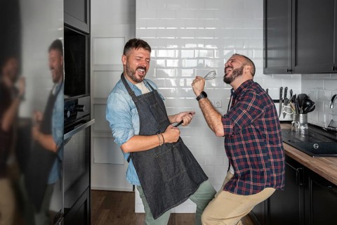 A cheerful gay couple enjoys a playful moment in their modern kitchen, passionately dancing and