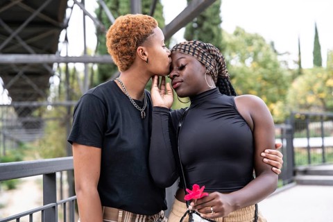 A loving LGBTQ multiethnic couple embraces in a park, sharing a tender moment. One partner gently
