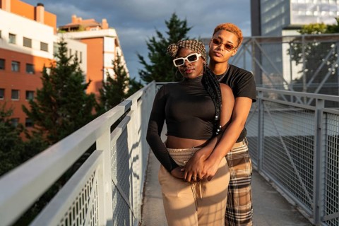 A loving LGBT multiethnic couple embraces warmly on a sunny urban bridge. They share a joyful and
