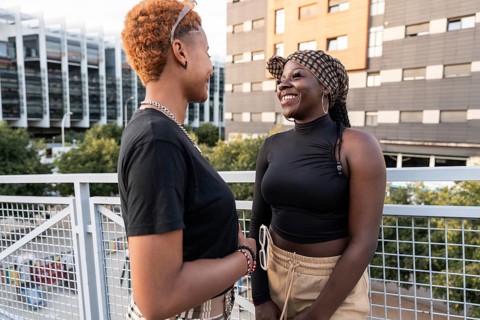 A joyful LGBT multiethnic couple shares a warm moment on a sunny day, standing on an urban terrace.