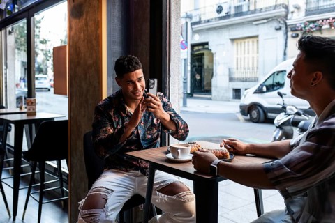 A latin gay couple enjoys coffee and pastries while sitting at a cafe. One partner is engaging with