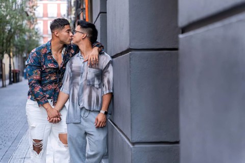A latin gay couple shares a tender kiss while holding hands in the vibrant streets of Madrid. The