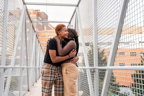 A joyful LGBT multiethnic couple shares a warm embrace on a metal walkway bridge, surrounded by