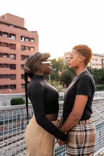A loving LGBT multiethnic couple stands closely, facing each other, on an outdoor walkway. The