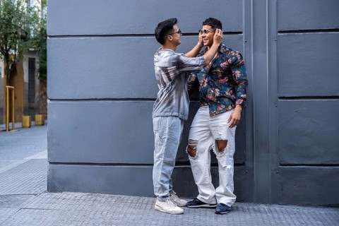 A latin gay couple enjoys a playful moment on an urban street, showing affection. They wear casual