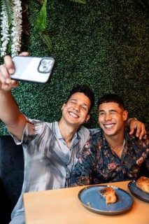 A joyful latin gay couple takes a selfie while enjoying brunch at a café. Their smiles and stylish